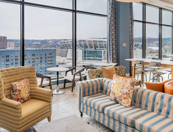 High-rise lounge with striped seating, floor-to-ceiling windows overlooking waterfront stadium and city skyline